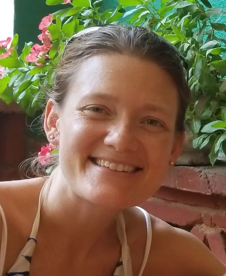 A smiling woman with dark hair pulled back, sitting outdoors.