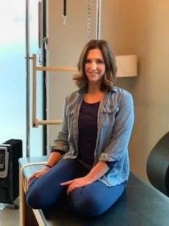 Woman with shoulder-length brown hair sitting cross-legged in pilates studio