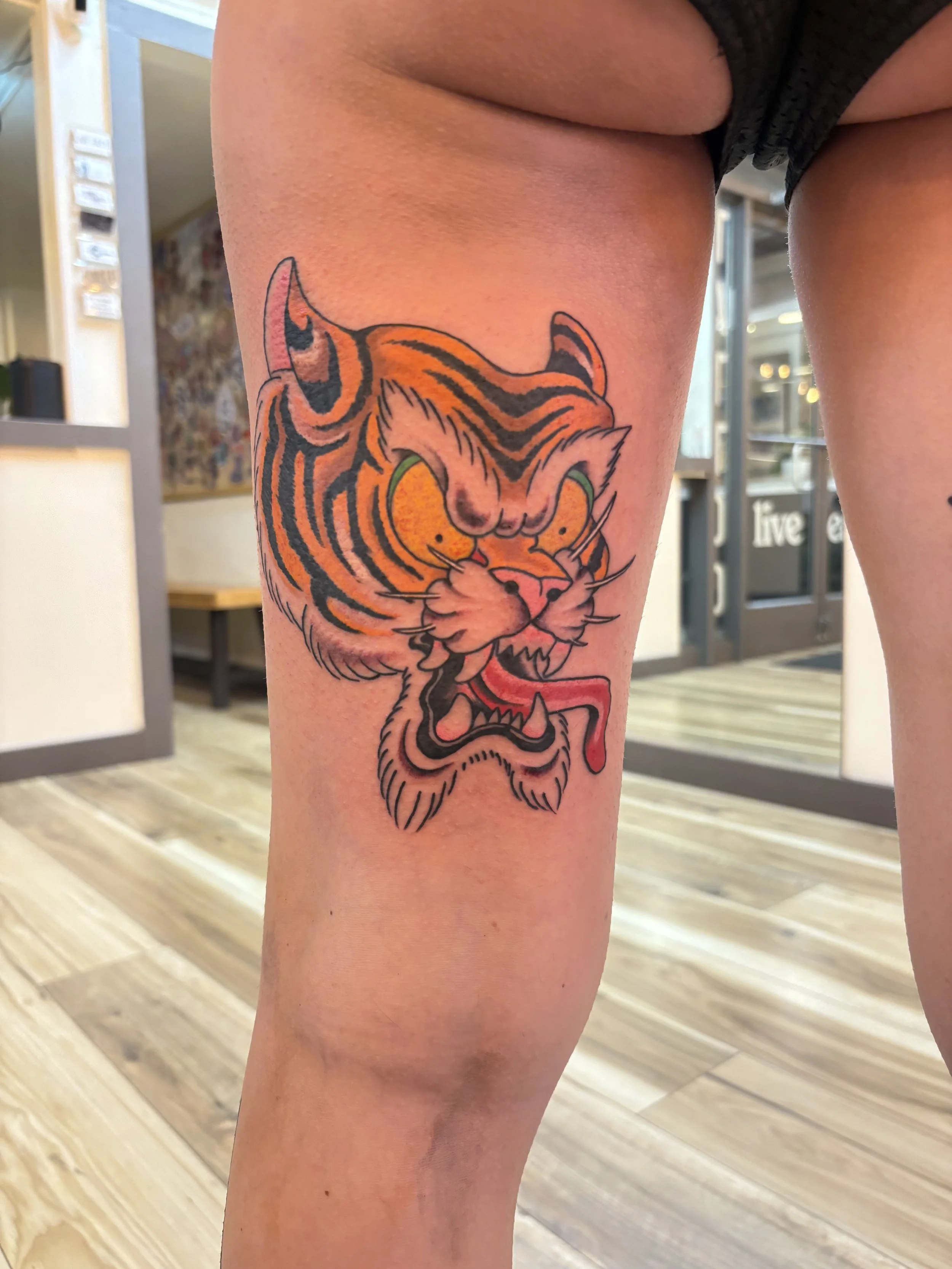 Tattoo of a tiger's face with orange and black stripes on a person's thigh.