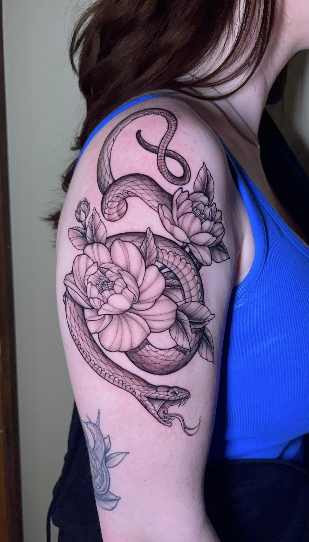Black and gray line tattoo of a serpent coiled around large flowers on a person's upper arm.