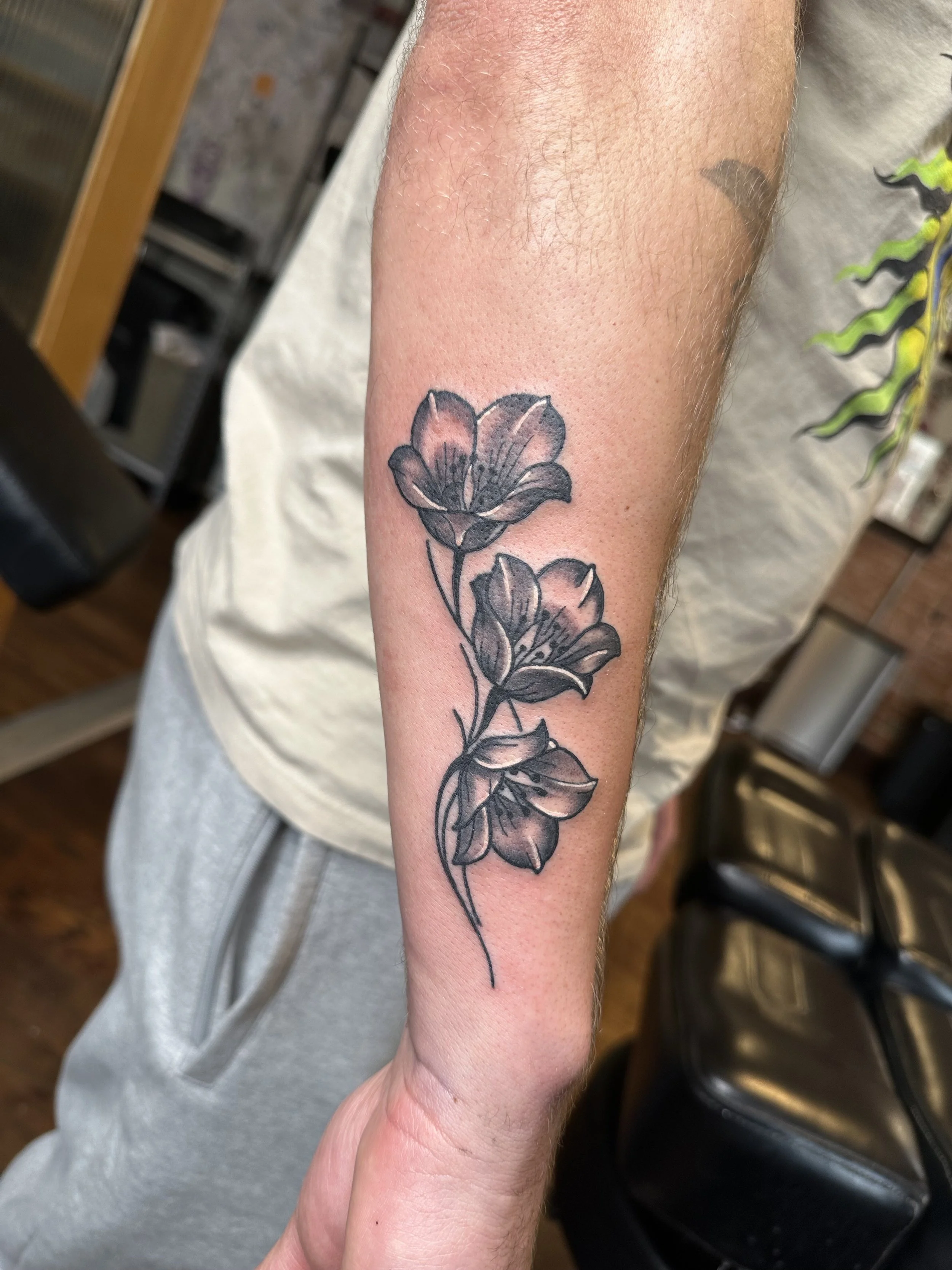 A person's forearm with a black floral tattoo featuring two blooming flowers on the arm.