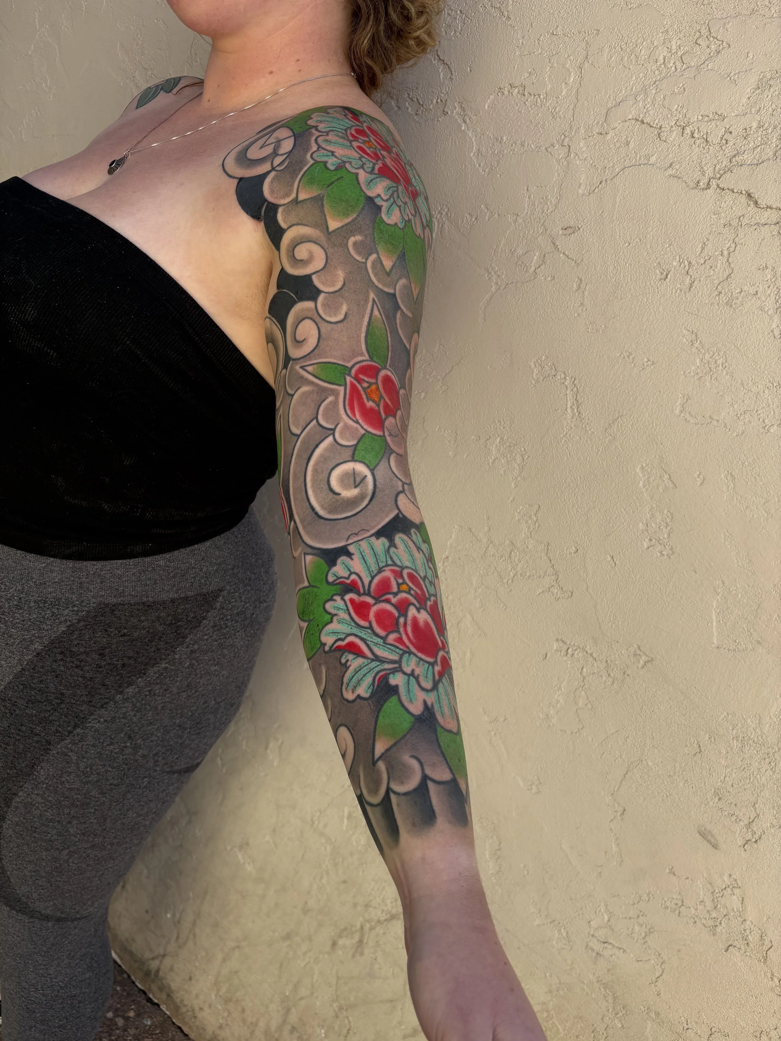 A person's arm with colorful floral tattoos, resting against a textured beige wall.