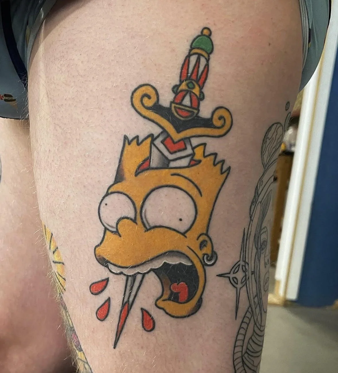 Colorful tattoo of Lisa Simpson with a push pin piercing through her forehead, with a decorative dagger on her head, on a person's arm.