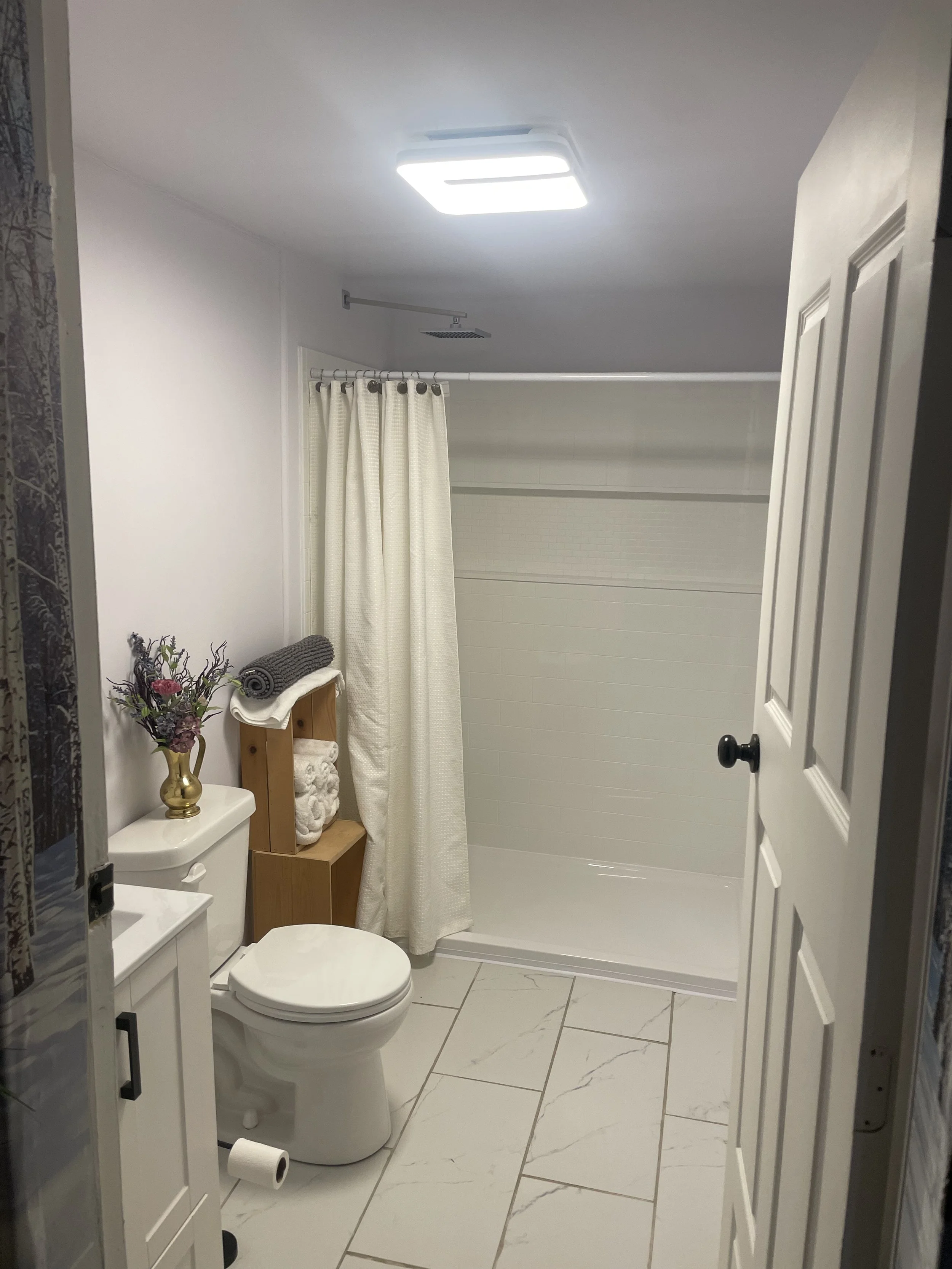 The private three‑quarter bathroom features a sink, toilet, and shower, with motion‑sensor lighting, an automatic fan, marble floors, a touch‑activated heated anti‑fog mirror, fresh towels, a clean bath mat, and house coats and slippers available upo