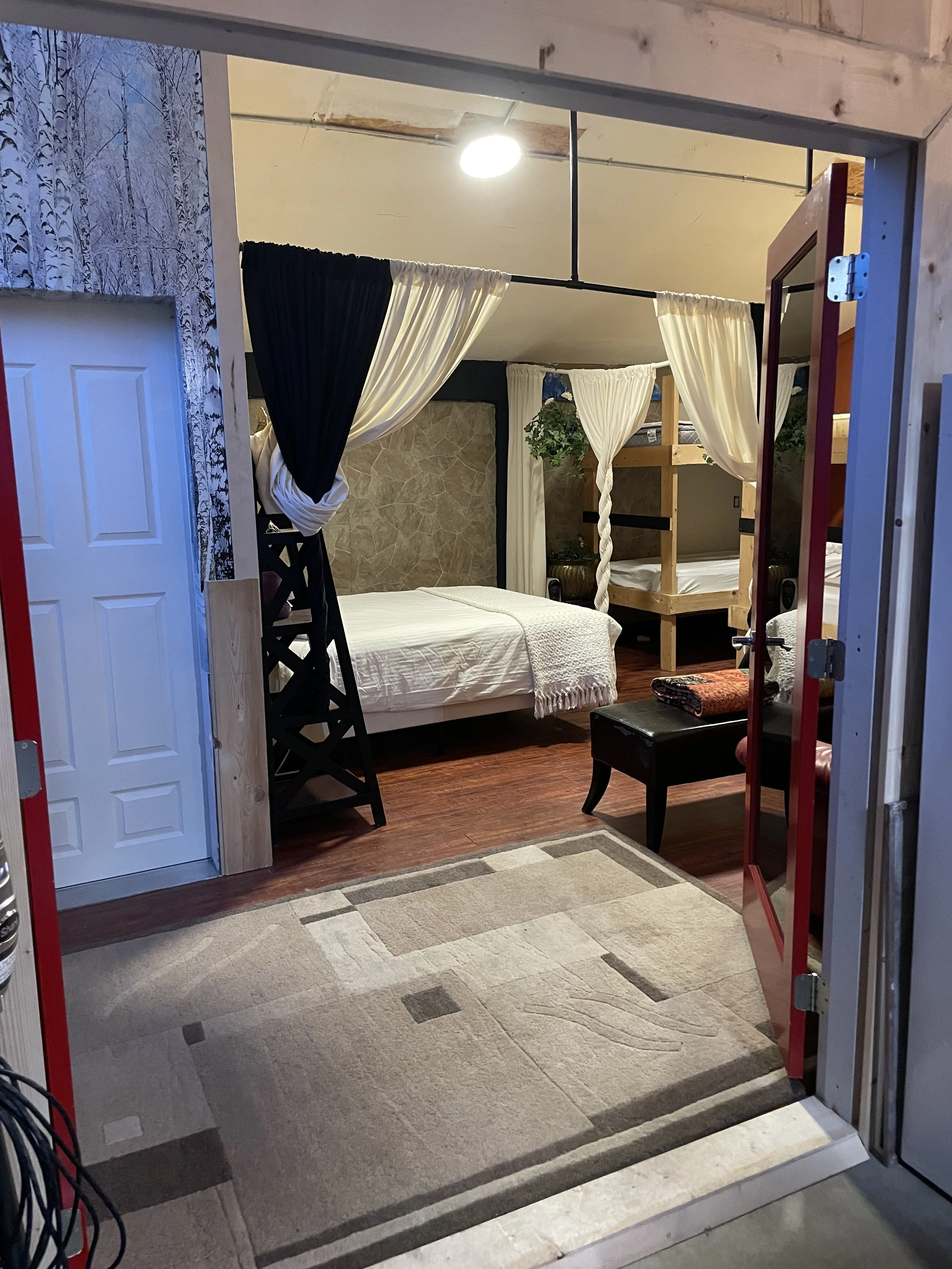 Through the red French doors, the private three‑quarter bathroom sits straight ahead, while the bunk room is just to the right. The bathroom includes a sink, toilet, and shower, with motion‑sensor lighting, an automatic fan, and marble floors.