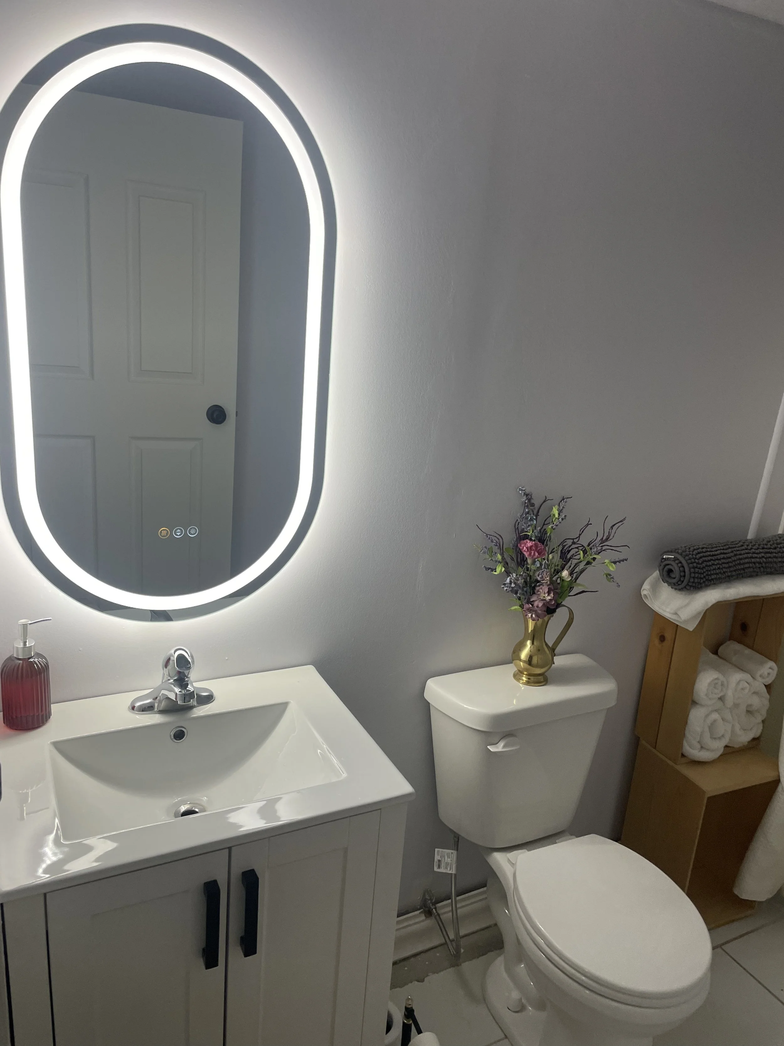 The private three‑quarter bathroom features a sink, toilet, and shower, with motion‑sensor lighting, an automatic fan, marble floors, a touch‑activated heated anti‑fog mirror, fresh towels, a clean bath mat, and house coats and slippers available upo