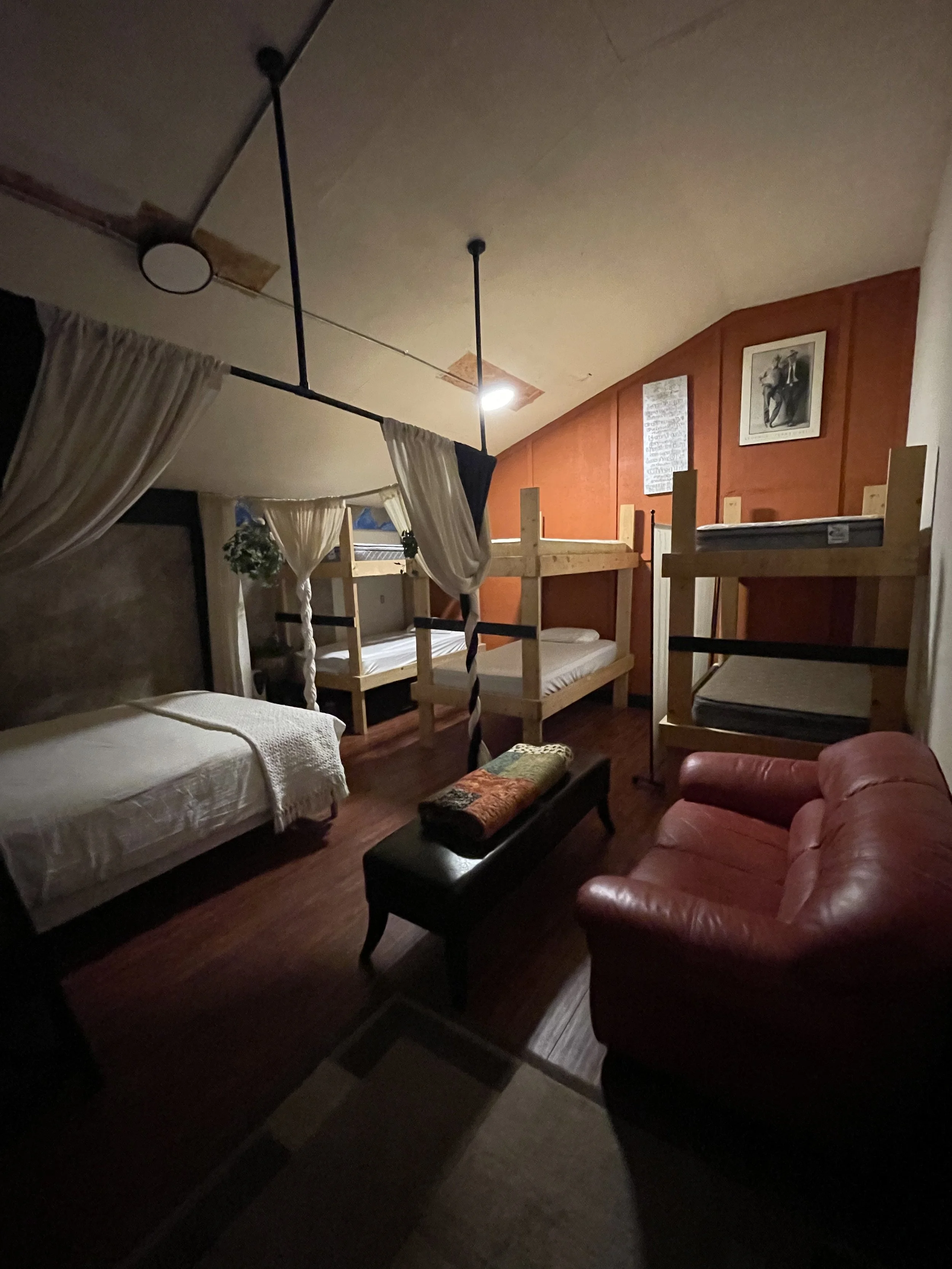 The bunk room features a queen bed with fresh sheets, a duvet with insert, four pillows, and soft privacy curtains that create a cozy retreat. The space also includes three cabin‑style bunk beds, each made up with fresh bedding and pillows, along wit