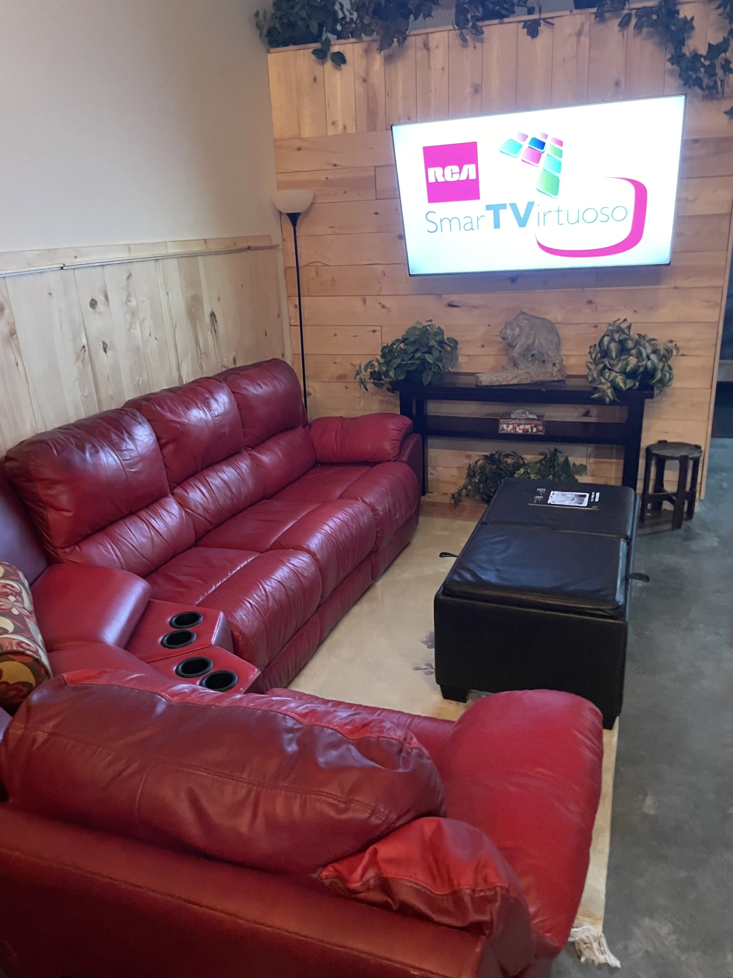 On the right, a red leather L‑shaped reclining sofa faces a 60‑inch smart TV, surrounded by cozy cabin shiplap walls