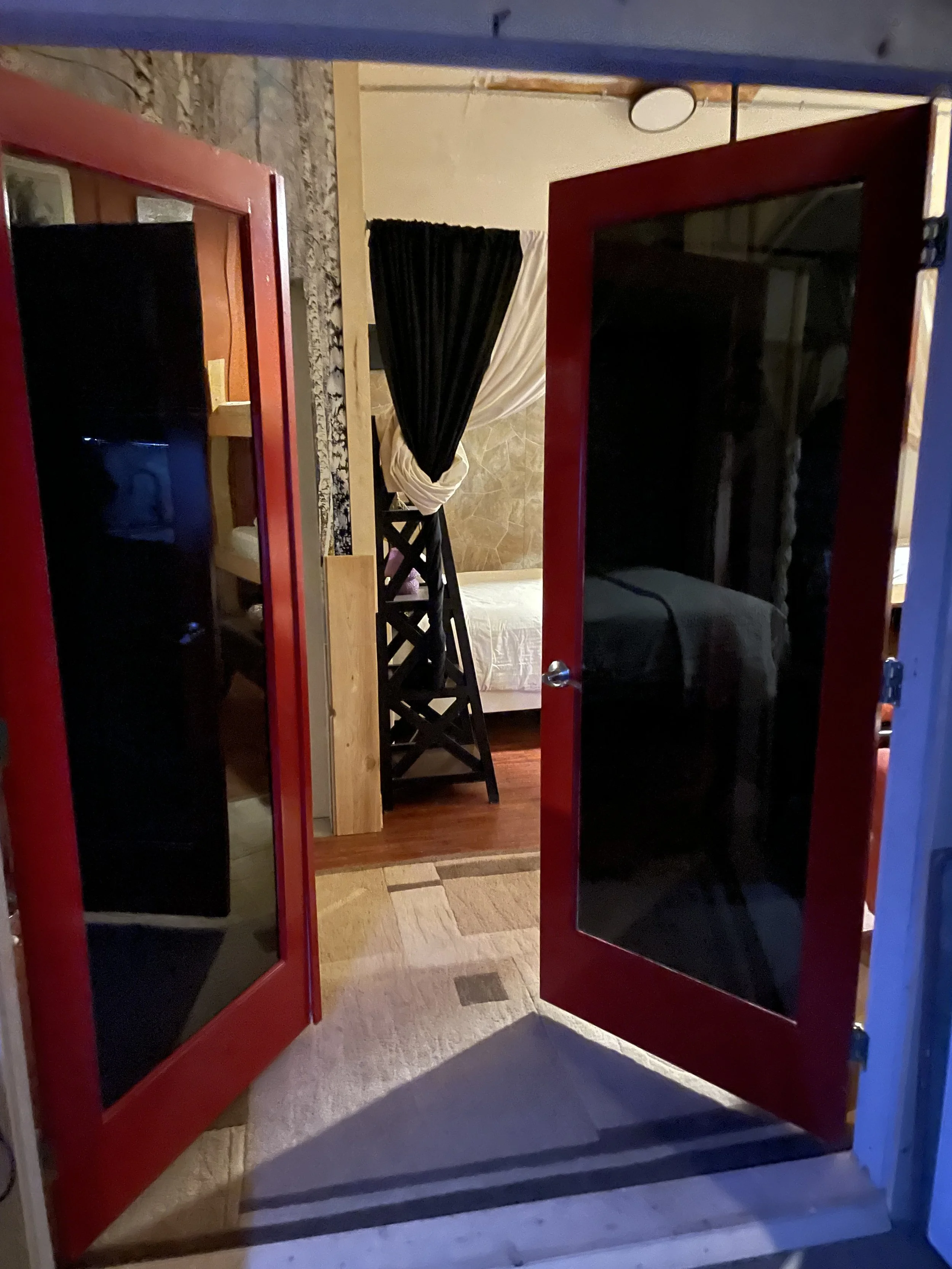 Through the red French doors, the private three‑quarter bathroom sits straight ahead, while the bunk room is just to the right.