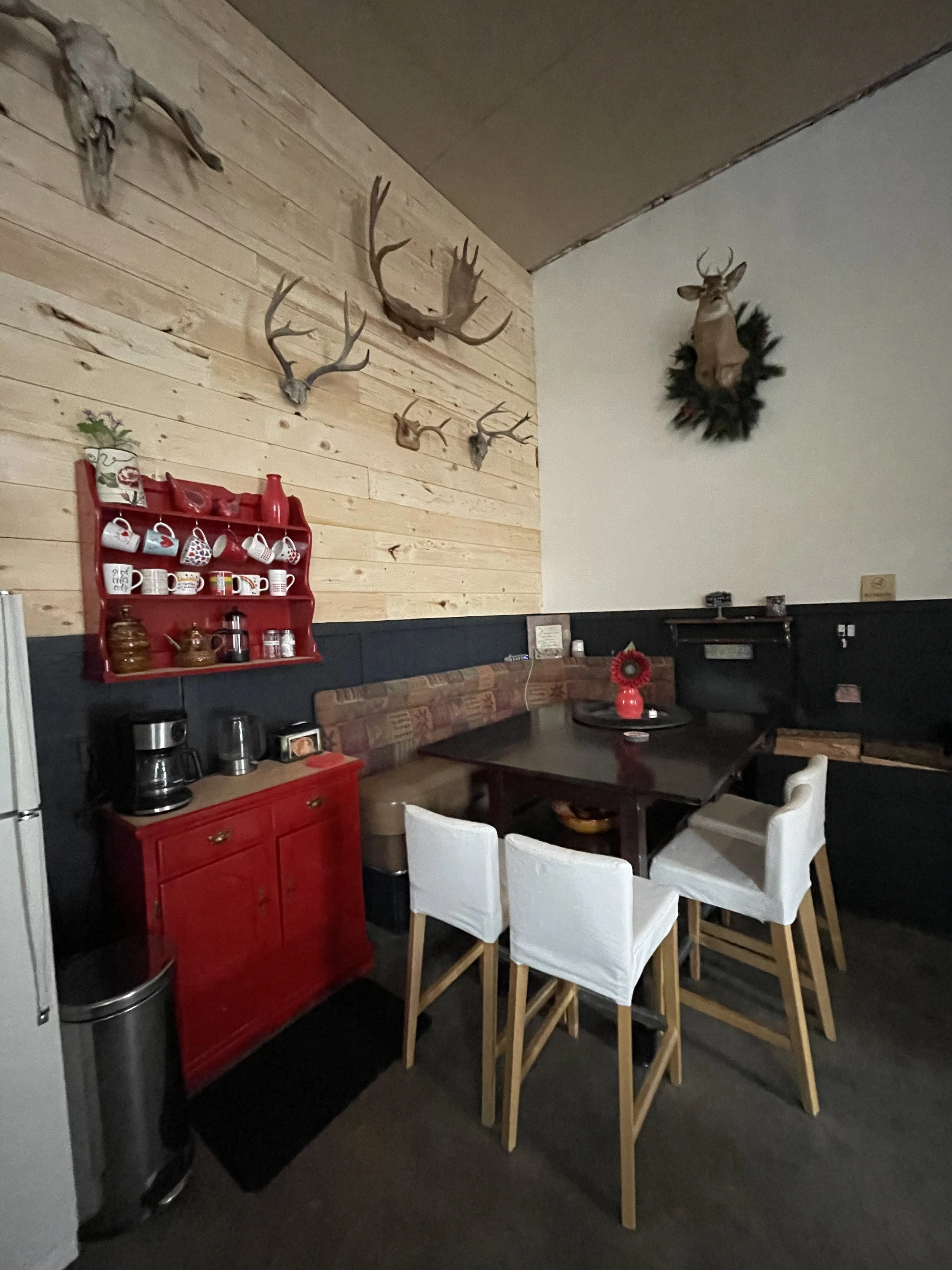 Opposite the kitchenette, a cozy breakfast nook feels like a warm mountain retreat — bar stools pulled up to a tall wooden table, ready for early‑morning plans or quiet evening chats. Just beside it, a fully stocked coffee station awaits, mugs lined 