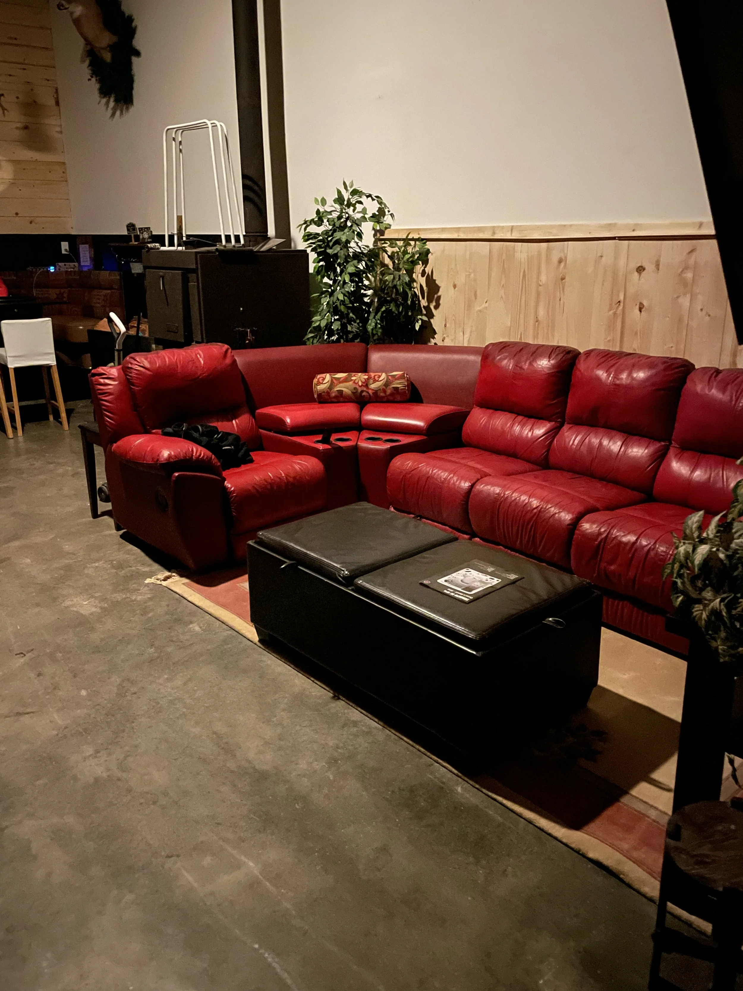 On the right, a red leather L‑shaped reclining sofa faces a 60‑inch smart TV, surrounded by cozy cabin shiplap walls