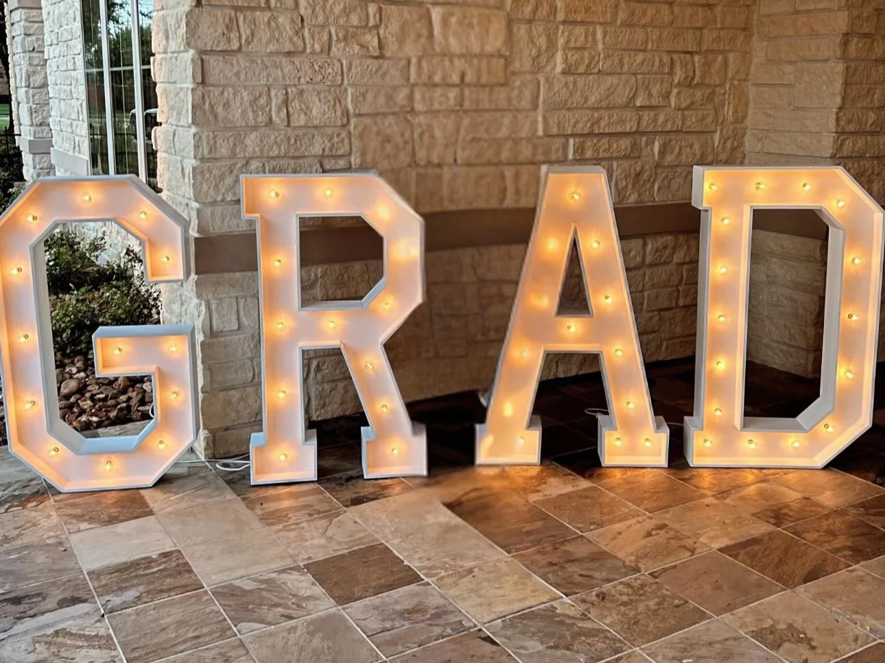 Large illuminated marquee letters spelling 'GRAD' placed on a tiled floor entry.