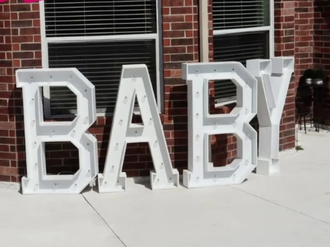 Large white decorative letters spelling out 'BABY' outside a brick house.