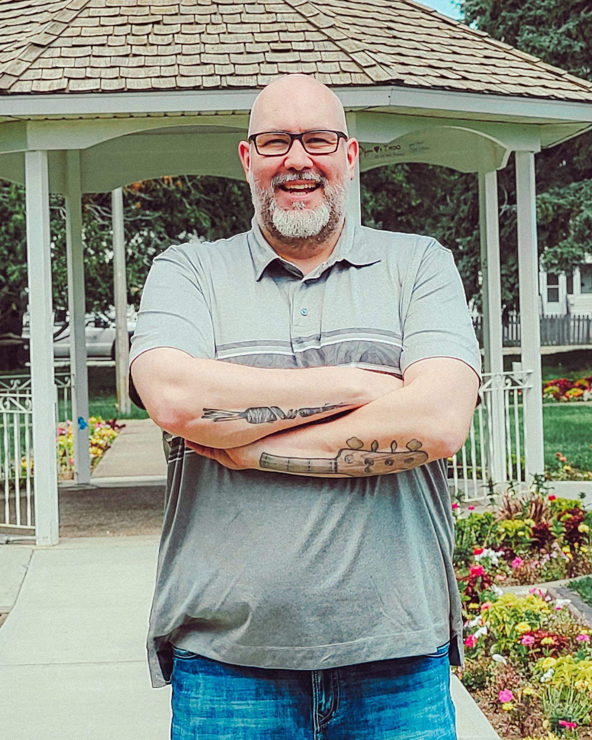 Adam Koch standing outdoors in Medicine Hat, in front of a gazebo and colourful flower beds.
