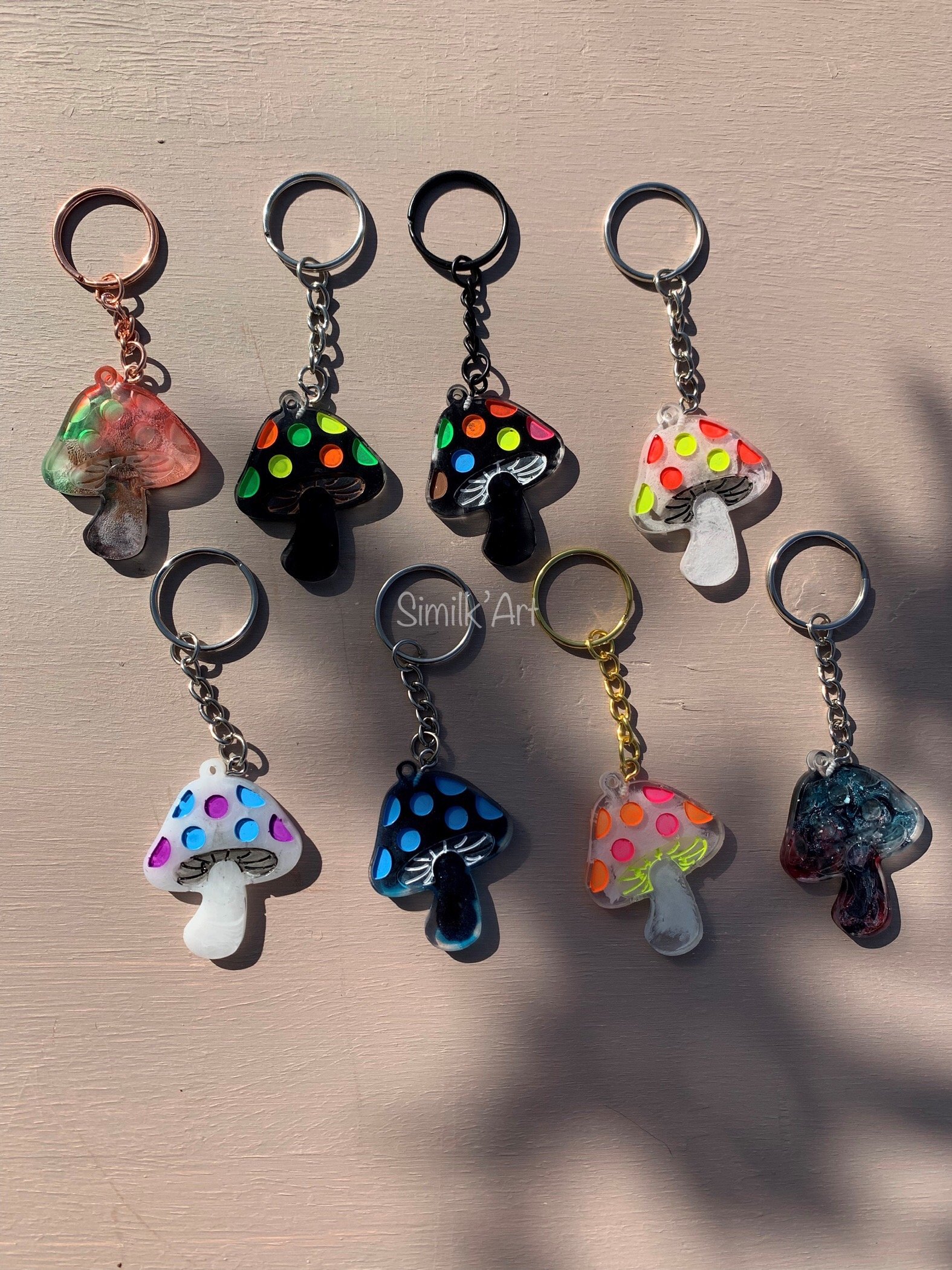 Collection of ten colourful mushroom-shaped keychains with various patterns, arranged on a beige surface.