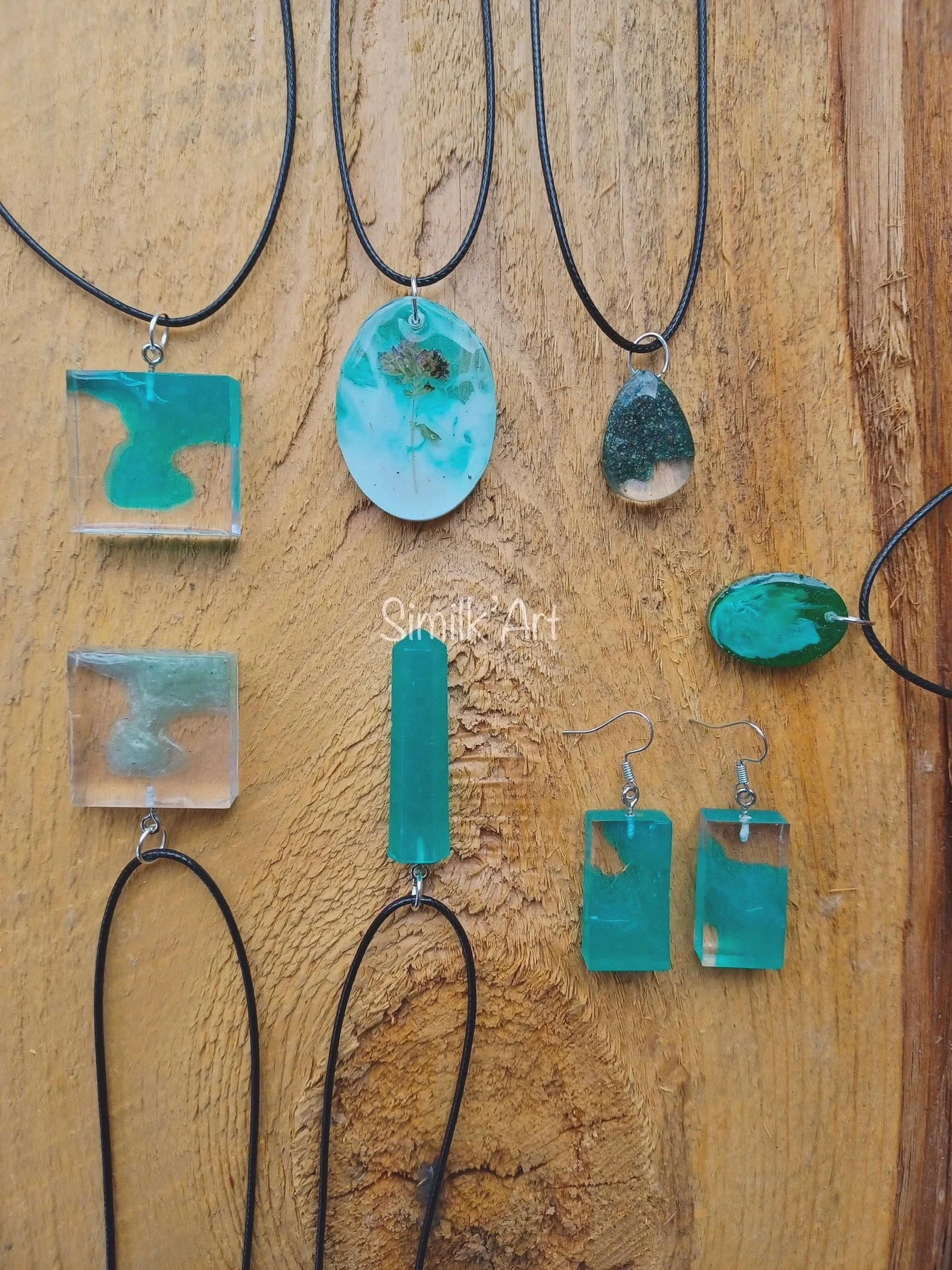 Collection of turquoise and green resin jewelry necklaces and earrings placed on a wooden background.