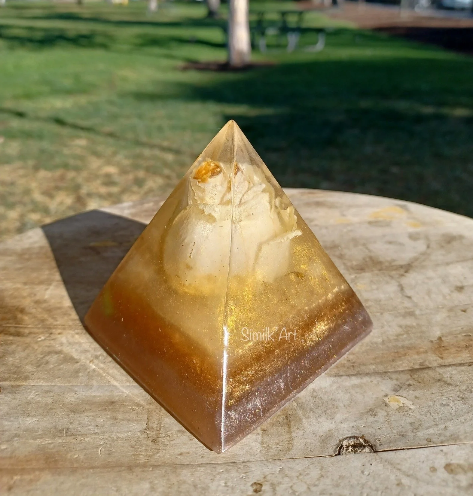 A yellow and brown resin pyramid with an embedded white rose placed in the middle of the piece.