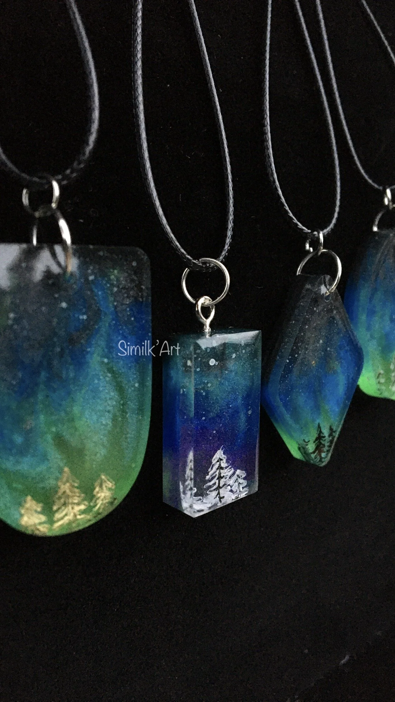 Necklaces with nature-themed pendant artwork of trees and northern lights
