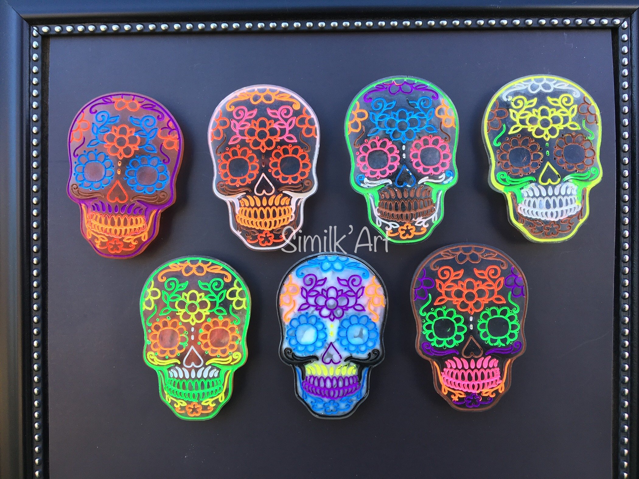 Set of seven neon-colored sugar skulls with floral designs on a black background.