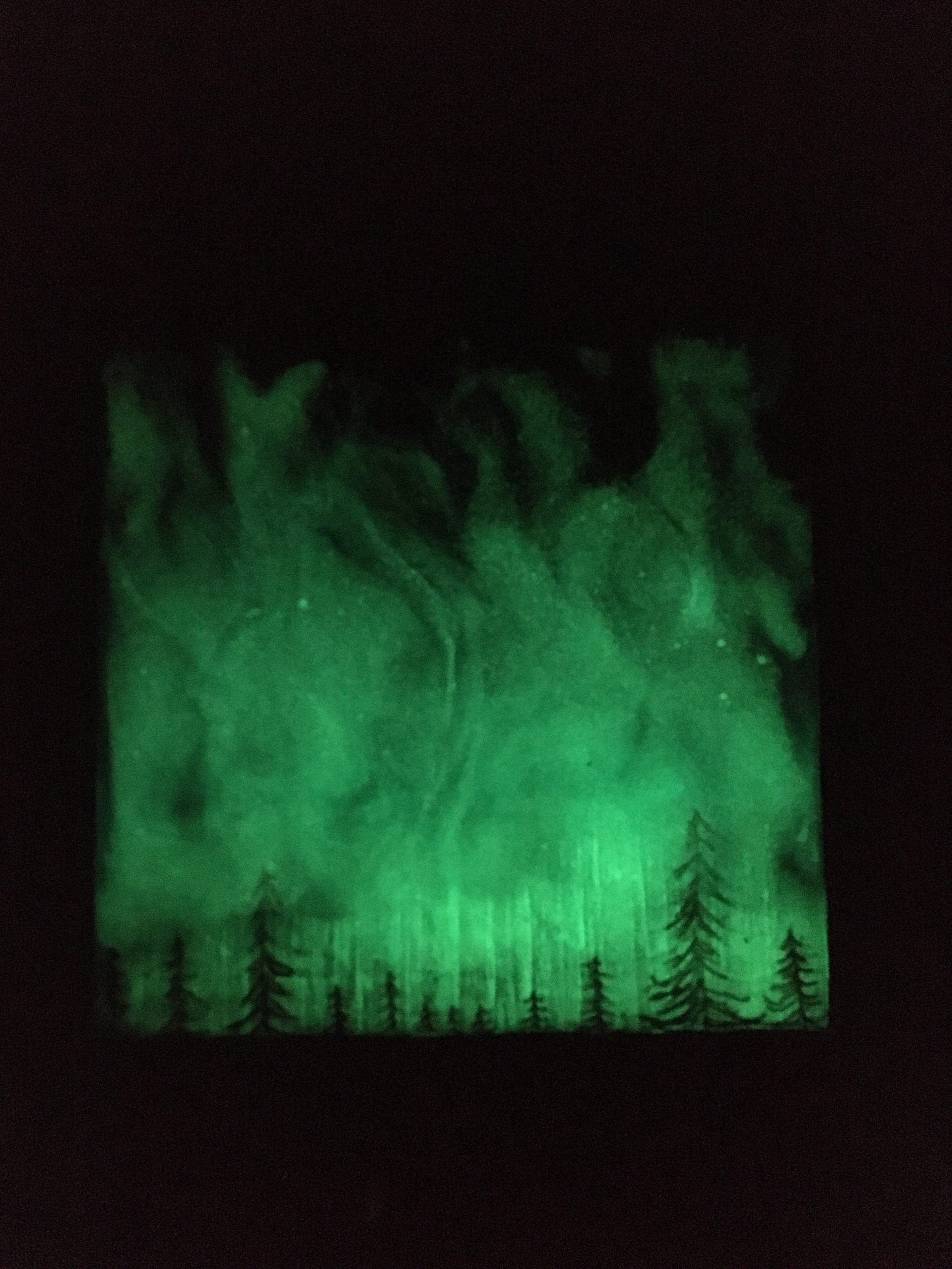 Glow-in-the-dark painting of green aurora borealis and silhouettes of pine trees at the bottom.