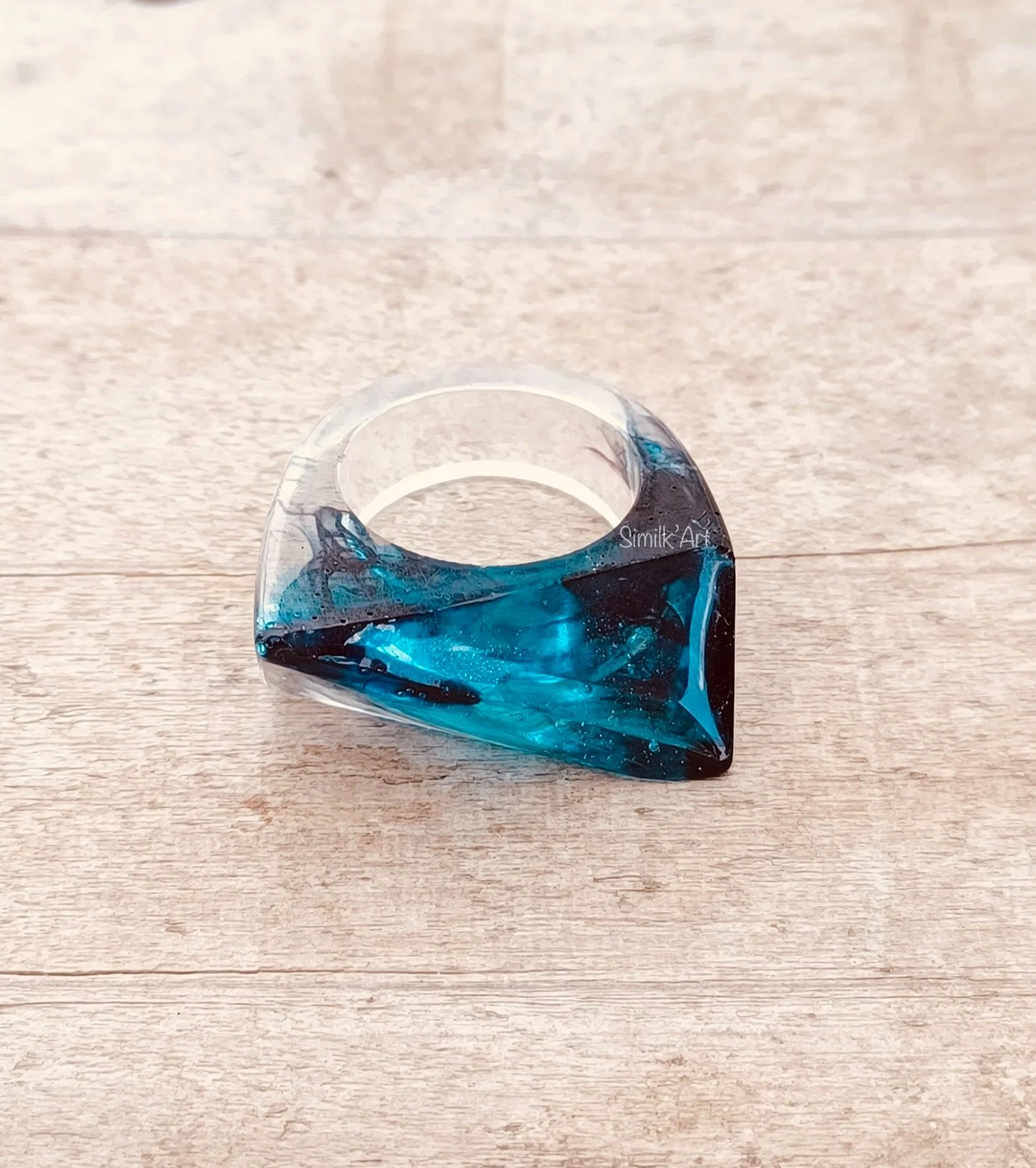 A chunky-shaped resin ring with black and blue galactic vibes , placed on a wooden surface.