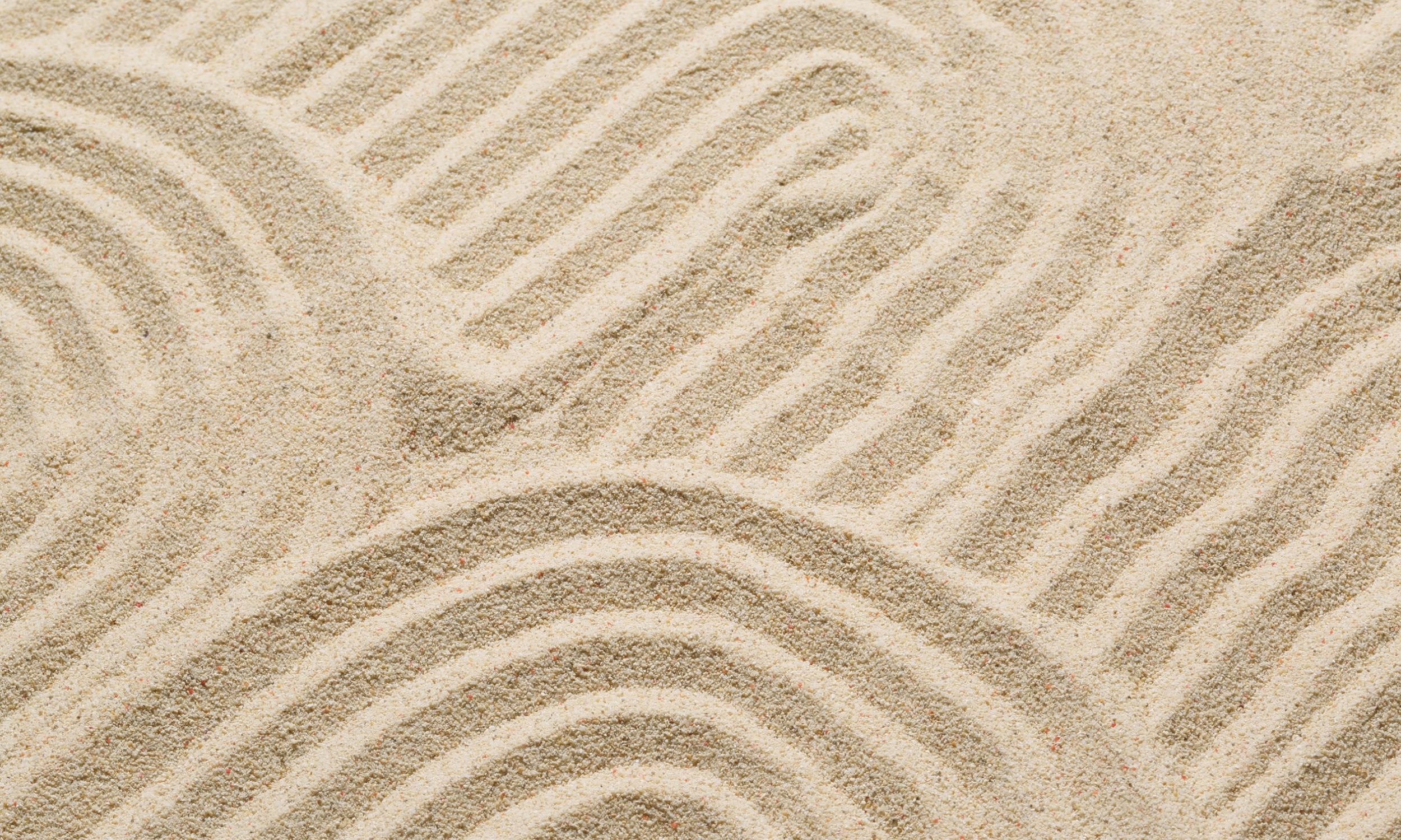 Close-up of sand with shallow grooves and patterns in a zen garden style.