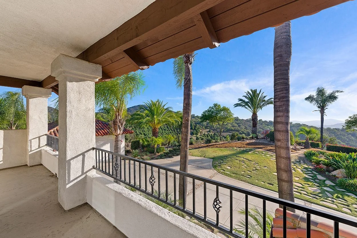 Balcony view overlooking a yard with palm trees, a lawn, and a clear blue sky.