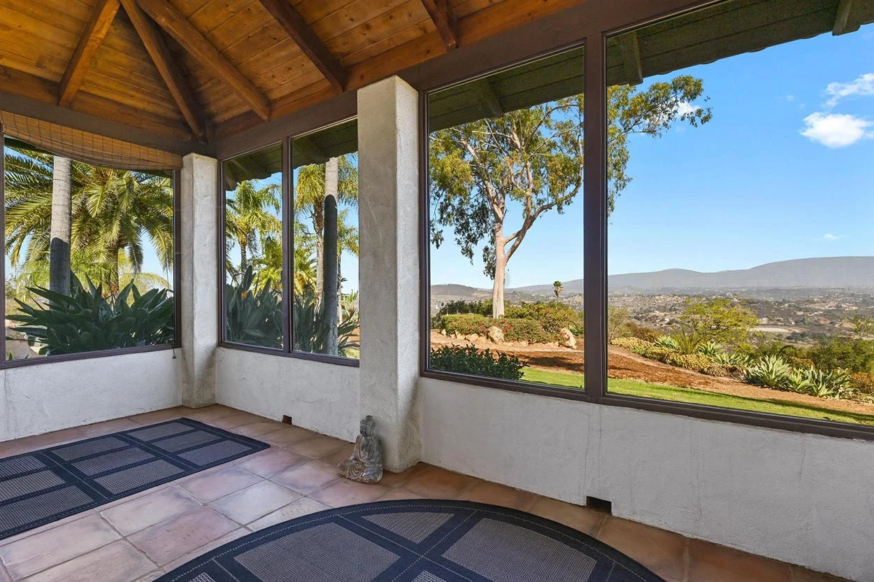 Sunroom with large windows showing a view of trees, plants, and mountains in the distance.