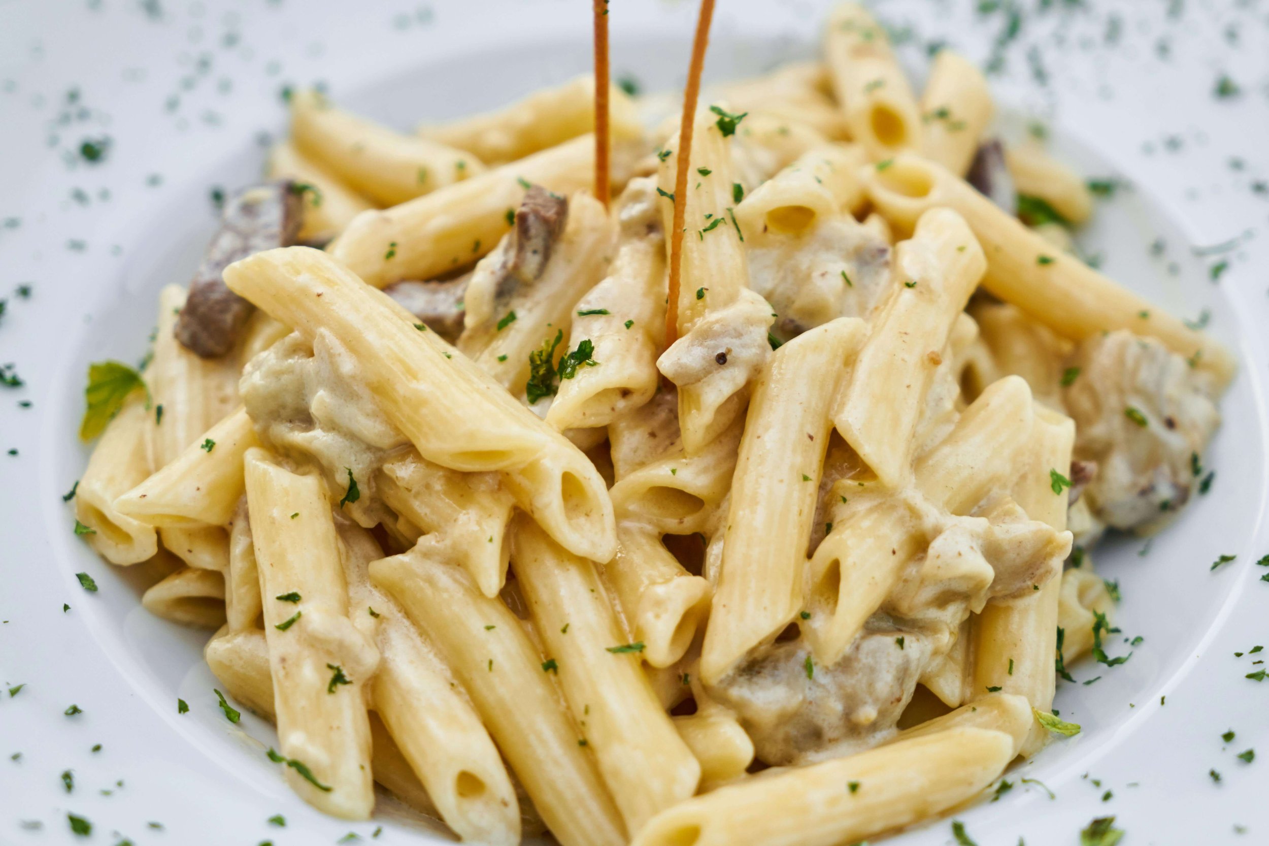 A plate of creamy chicken Alfredo pasta with penne noodles, pieces of chicken, and herbs, garnished with parsley.
