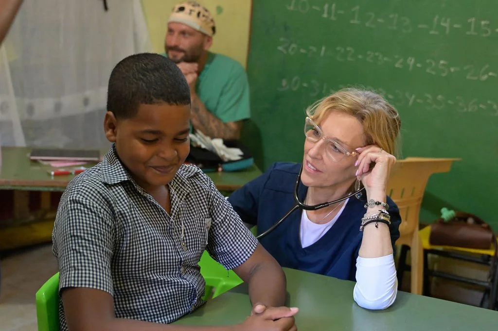 Healthier Futures International volunteer sits with a smiling boy in a classroom during 2026 medical mission