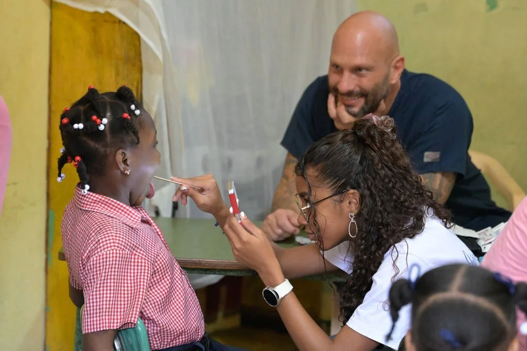Healthier Futures International volunteer examines a girl using a tongue depressor at 2026 community clinic
