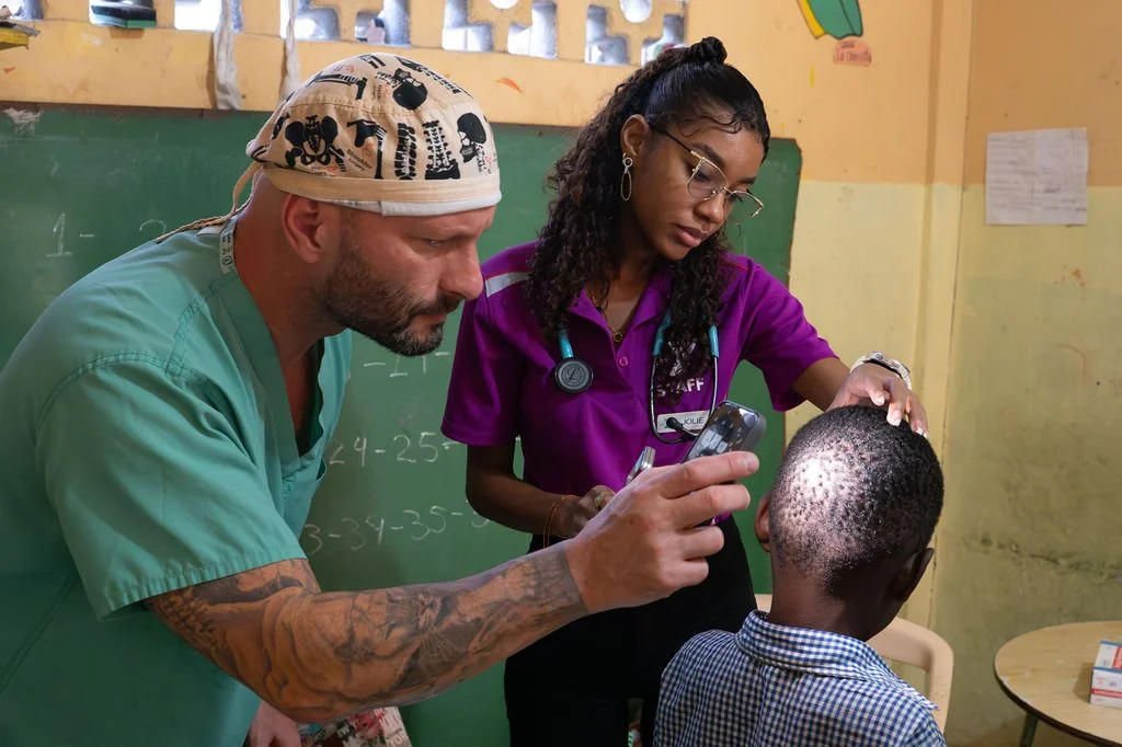Healthier Futures International volunteers in scrubs use a light to examine a child's ear at 2026 mission