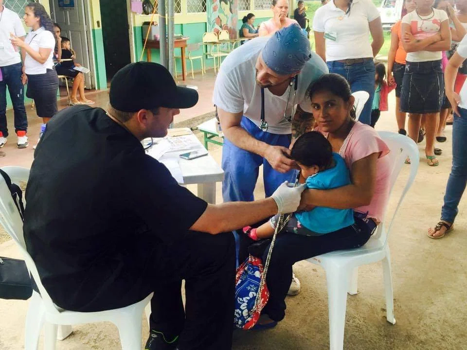 Healthier Futures International volunteer examines a young child with a stethoscope at 2015 community clinic