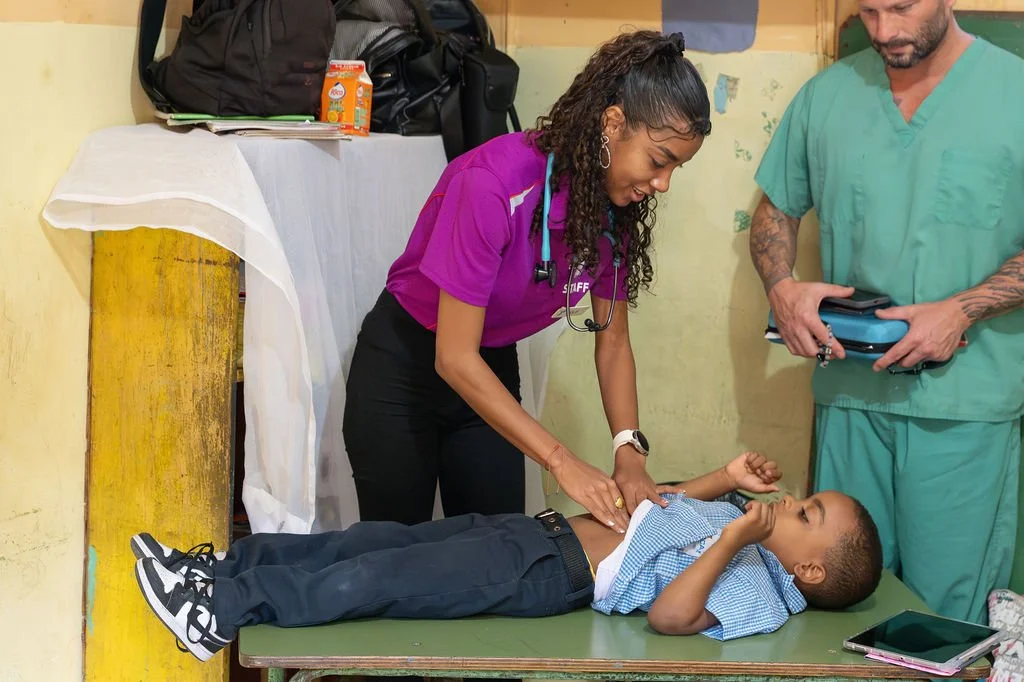 Healthier Futures International volunteer in scrubs examines a young child on a table during 2026 mission