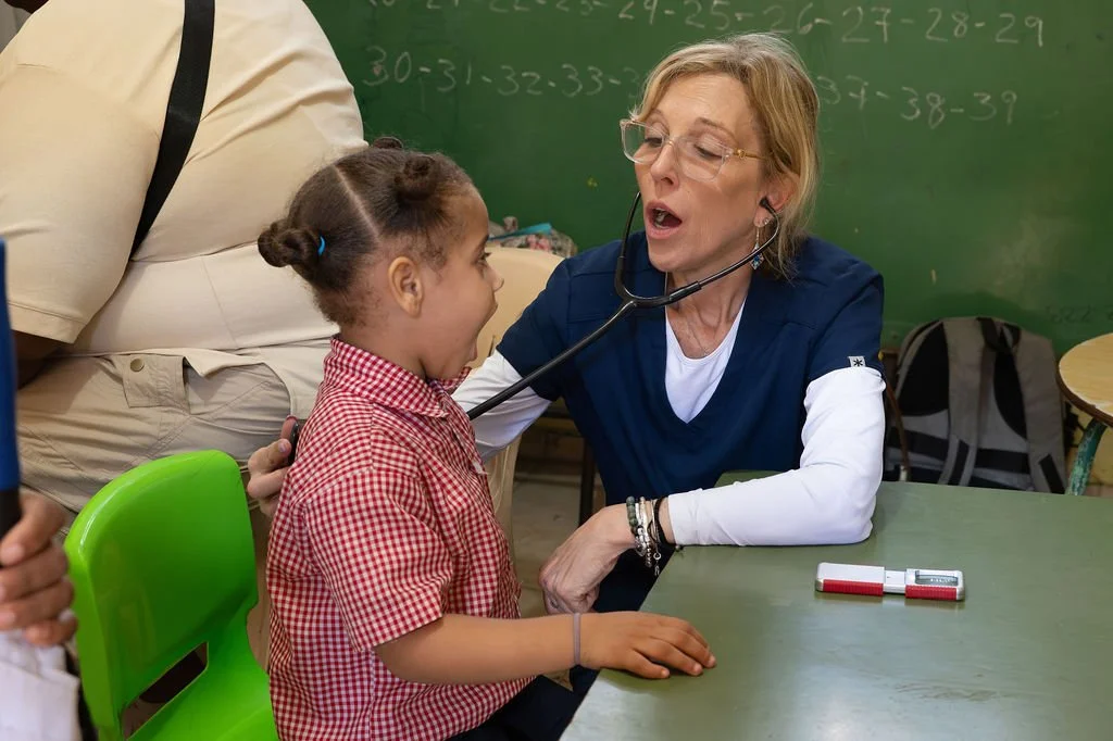 Healthier Futures International volunteer listens to a young girl's breathing with a stethoscope at 2026 clinic