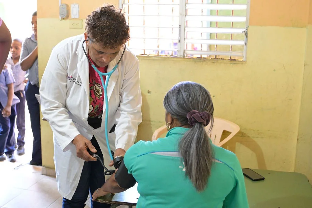 Healthier Futures International volunteer in a lab coat takes a patient's blood pressure at 2026 clinic