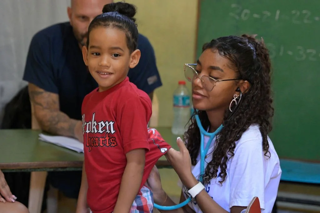 Smiling child is examined by a Healthier Futures International volunteer with a stethoscope at 2026 clinic