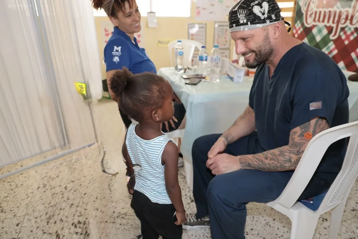 Healthier Futures International volunteer in scrubs greets a young child at 2024 community health clinic