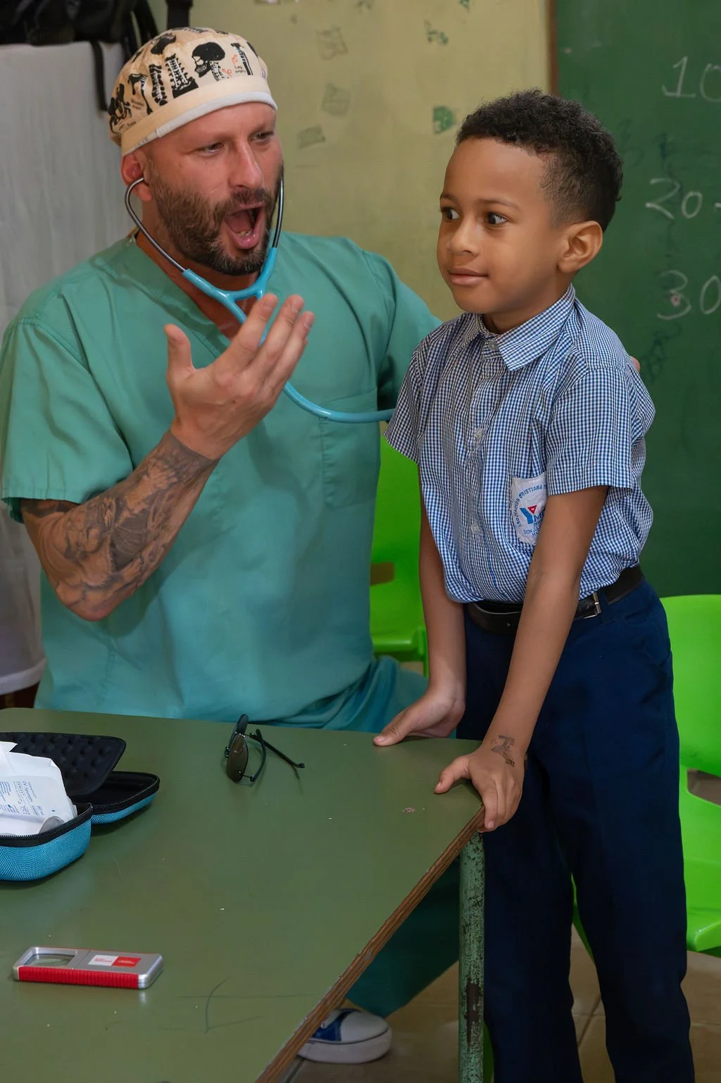 Healthier Futures International volunteer in scrubs makes a child laugh during an exam at 2026 medical mission