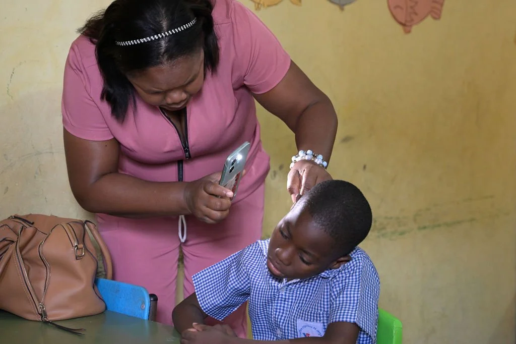 Healthier Futures International volunteer examines a child's scalp with a light at 2026 community clinic