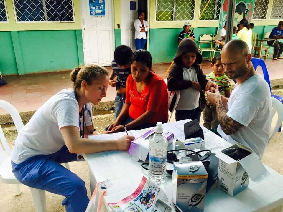 Healthier Futures International volunteer records patient information at an outdoor community health clinic in 2015