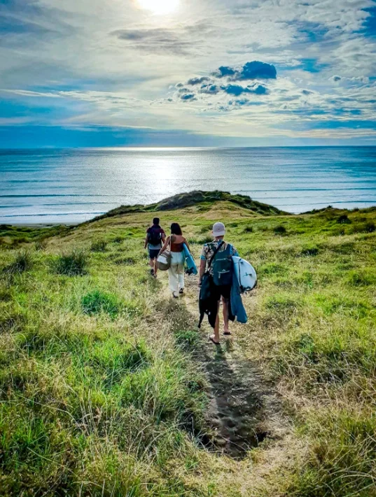 3 amigos caminando por el campo con tablas de surf con direccion a la playa
