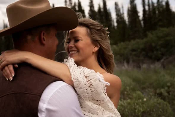 A couple sharing a kiss outdoors in a natural setting with trees in the background with a perfect spray tan.