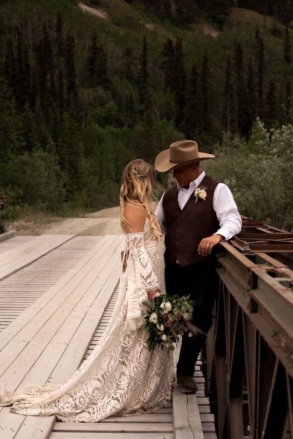 A bride and groom sharing a tender moment on a rustic wooden bridge in a forested area during a wedding with a perfect spray tan.