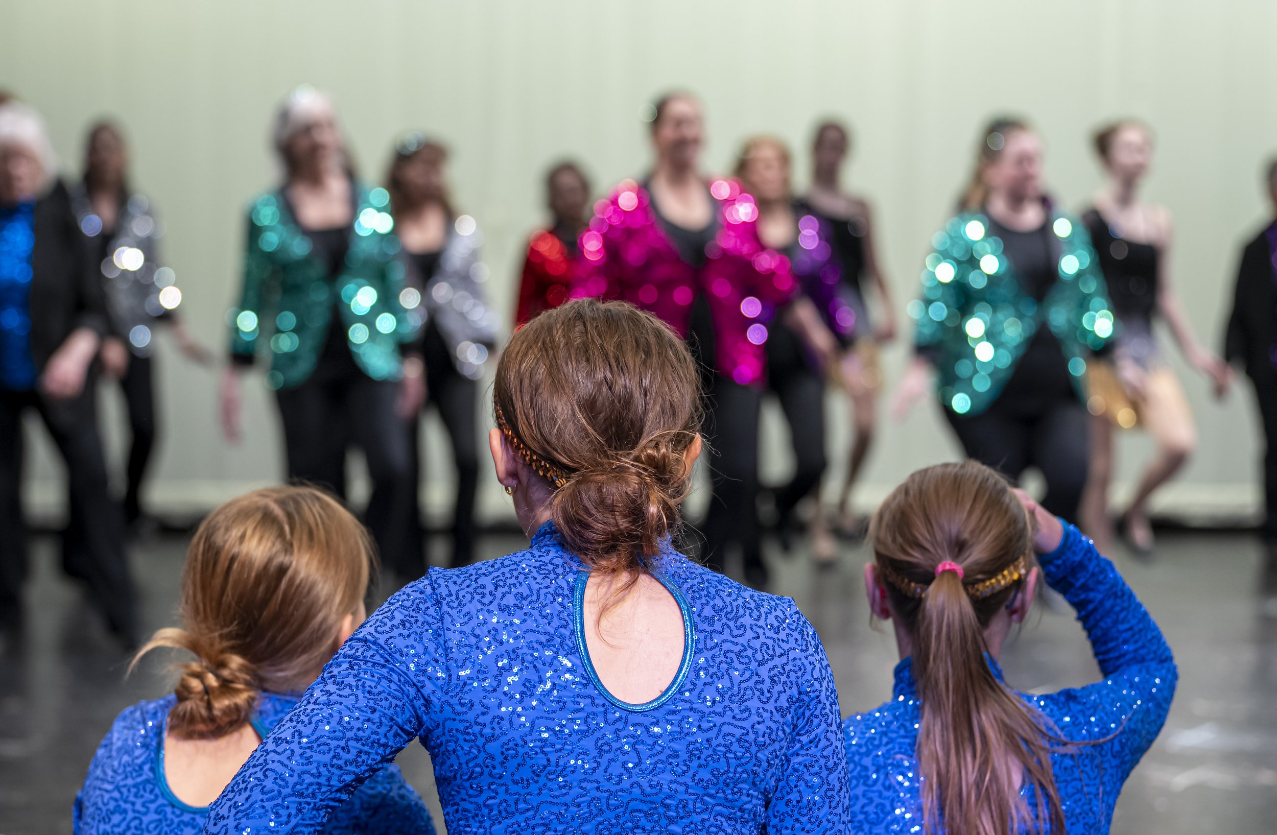 Three young women watching women perform at a dance recital