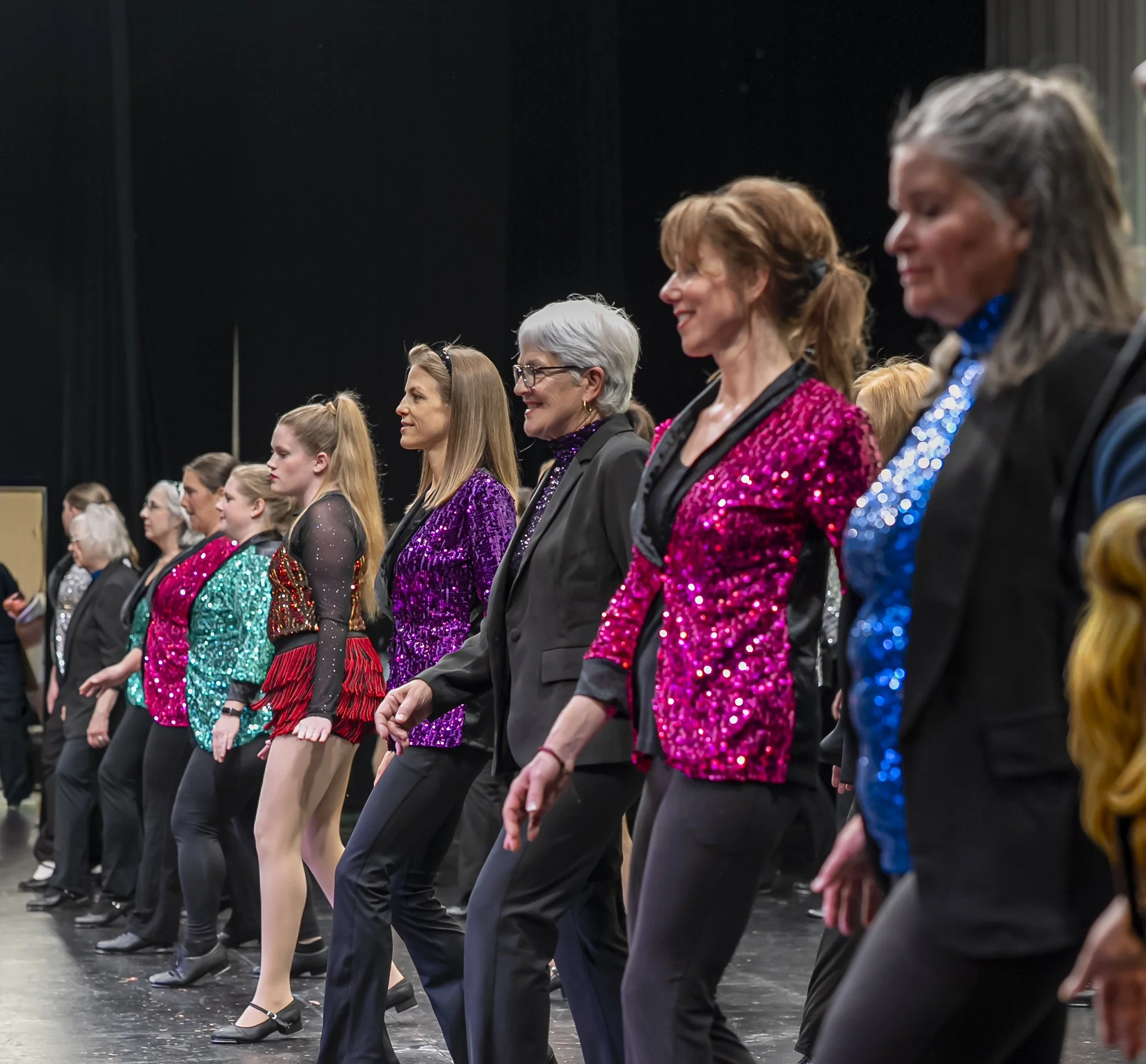 A row of women in sequined jackets performing at a dance recital