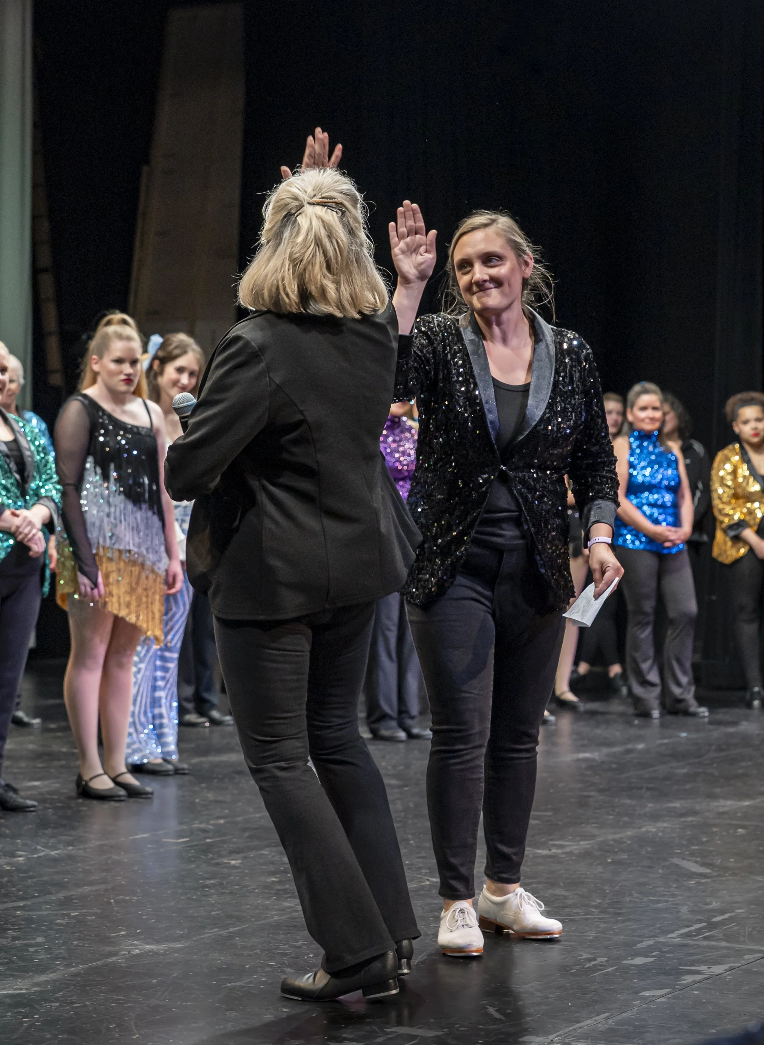Two women high-fiving in front of their dance recital students