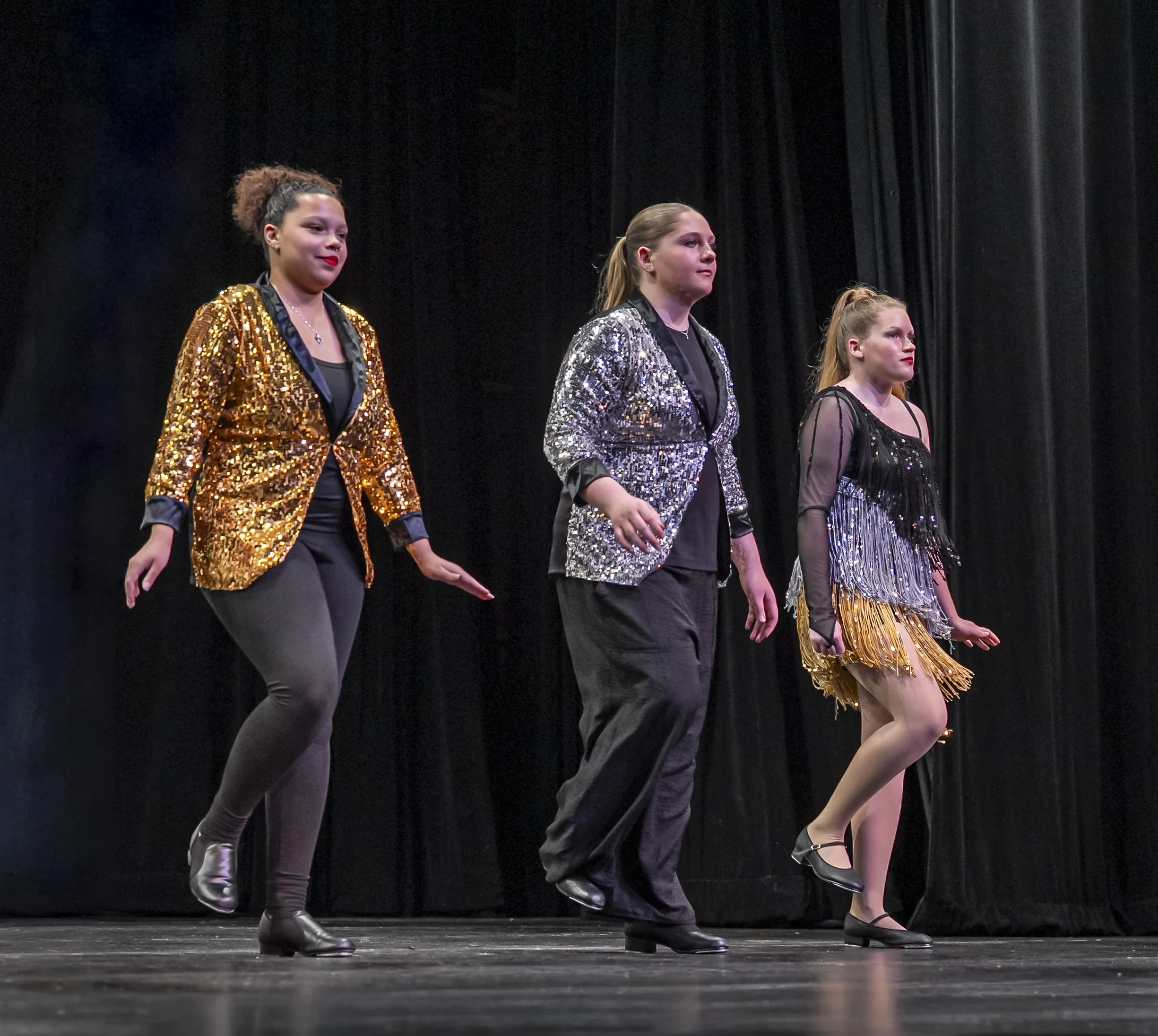 Three teenage-aged girls in sequined jackets performing at a dance recital