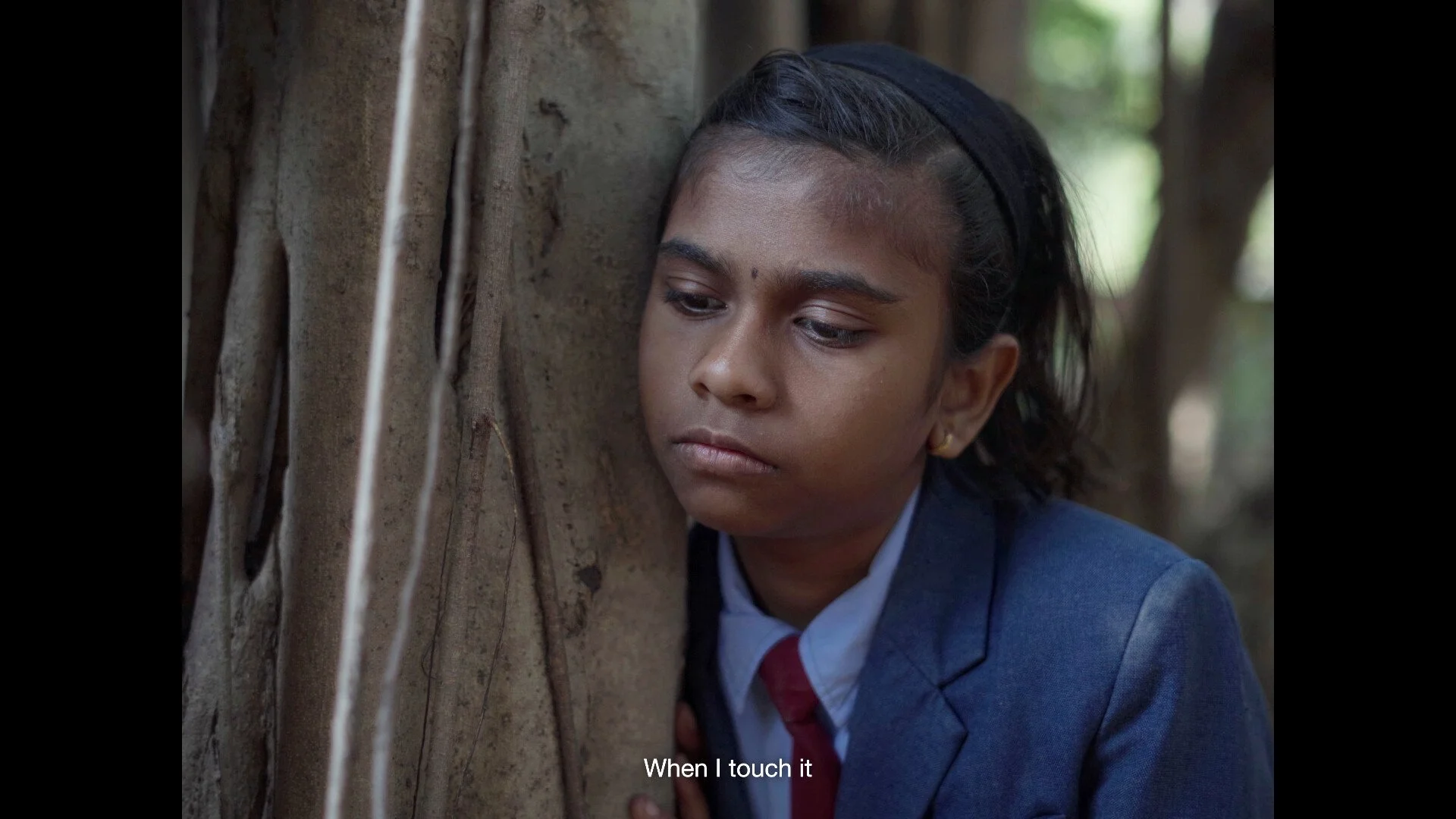 An Indian schoolgirl hugs a large tree