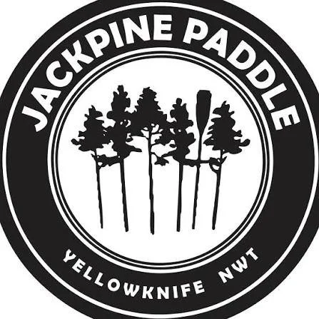 Logo for Jackpine Paddle with a circular design featuring five pine trees in the center and text around the edge that reads "Jackpine Paddle" at the top and "Yellowknife NWT" at the bottom.